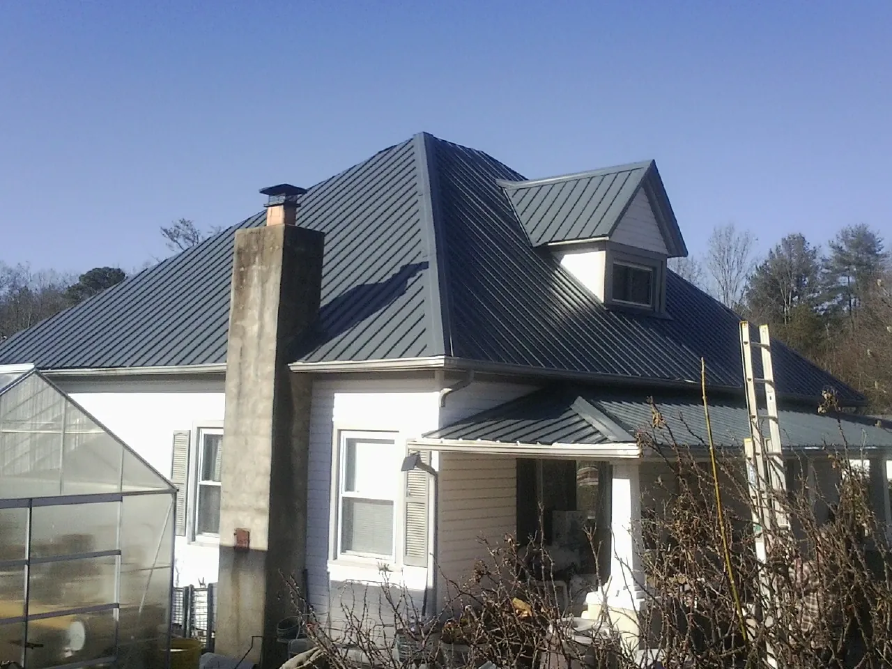 Dark blue standing seam metal roof on a white farmhouse with dormer — Slate & Tile Roof Repair by Roofing Brothers in Oakdale