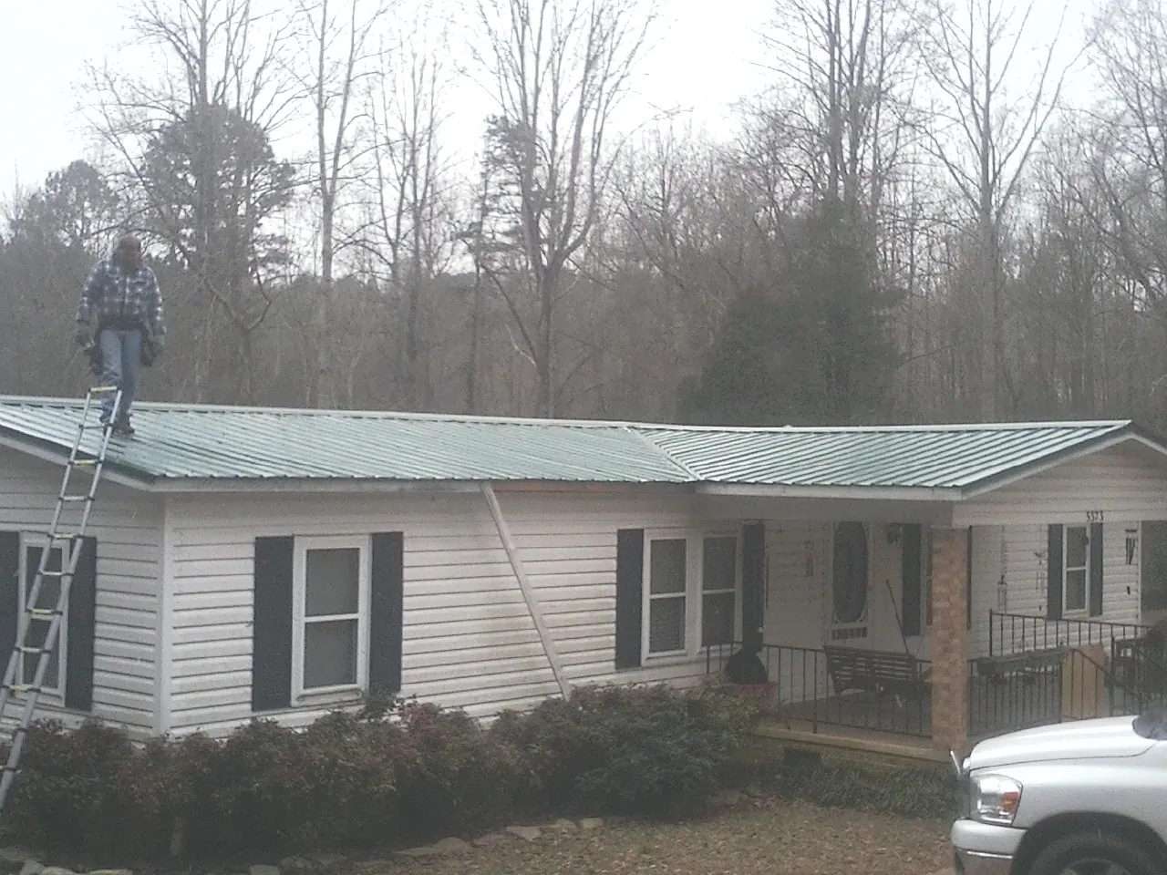 Worker on a ladder beside a new green metal roof on a ranch home in Oakdale